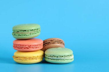 Çok sayıda renkli badem kurabiyesi yakından çekilmiş. Mavi arka planda parlak Fransız badem kurabiyeleri, yan manzara. Farklı aromalı makaron çeşitleri. Lezzetli hamur işleri, kurabiyeler, yemek geçmişi. Bir yığın tatlı.