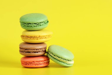 Renkli kurabiyeler yığını, yakın plan. Sarı arka planda parlak Fransız badem kurabiyeleri, yan görüş. Farklı aromalı makaron çeşitleri. Lezzetli hamur işleri, kurabiyeler, yemek geçmişi. Şeker kulesi