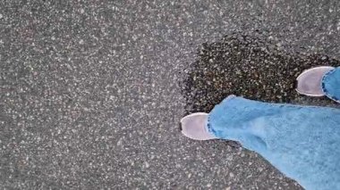 Islak asfalt üzerinde yürüyen insan ayaklarının yakın çekimi. Yağmurlu havada yürüyorum. Yürüyüş. Geniş mavi kotlu ve spor ayakkabılı kadın bacakları sokakta yürüyor, ilk bakışta. Yağmurda yürüyorum