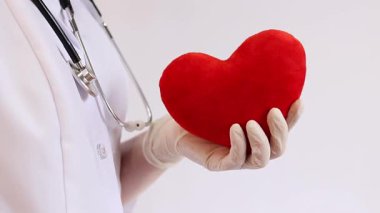 Bir kardiyologun ellerinde yumuşak yumuşak bir kalp. Tıbbi eldivenler içindeki doktorun elinde oyuncak kırmızı bir kalp var, yakın plan. Kalp bir doktorun ellerindedir. Sağlık ve Tıp Konsepti