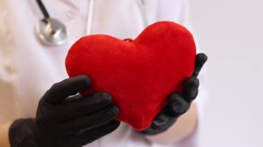 Bir kardiyologun ellerinde yumuşak yumuşak bir kalp. Tıbbi eldivenler içindeki doktorun elinde oyuncak kırmızı bir kalp var, yakın plan. Kalp bir doktorun ellerindedir. Sağlık ve Tıp Konsepti