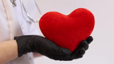Bir kardiyologun ellerinde yumuşak yumuşak bir kalp. Tıbbi eldivenler içindeki doktorun elinde oyuncak kırmızı bir kalp var, yakın plan. Kalp bir doktorun ellerindedir. Sağlık ve Tıp Konsepti