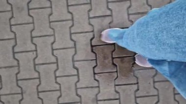 Kiremit kaplı bir yolda yürüyen insan bacaklarının yakın çekimi. Yağmurlu havada yürüyorum. Yürüyüş. Geniş mavi kot ve spor ayakkabılı kadın bacakları sokakta yürüyor, ilk bakışta görülüyor. Yağmurda yürüyorum