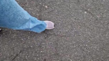 Islak asfalt üzerinde yürüyen insan ayaklarının yakın çekimi. Yağmurlu havada yürüyorum. Yürüyüş. Geniş mavi kotlu ve spor ayakkabılı kadın bacakları sokakta yürüyor, ilk bakışta. Yağmurda yürüyorum