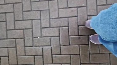 Kiremit kaplı bir yolda yürüyen insan bacaklarının yakın çekimi. Yağmurlu havada yürüyorum. Yürüyüş. Geniş mavi kot ve spor ayakkabılı kadın bacakları sokakta yürüyor, ilk bakışta görülüyor. Yağmurda yürüyorum