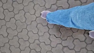 Kiremit kaplı bir yolda yürüyen insan bacaklarının yakın çekimi. Yağmurlu havada yürüyorum. Yürüyüş. Geniş mavi kot ve spor ayakkabılı kadın bacakları sokakta yürüyor, ilk bakışta görülüyor. Yağmurda yürüyorum