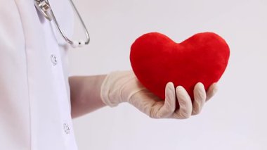 Doktorun ellerinde kırmızı peluş kalp. Kardiyoloji. Tıbbi eldivenler içindeki doktorun elinde oyuncak yumuşak bir kalp var. Yakın plan. Kalp doktorun ellerinde. Sağlık ve Tıp Konsepti