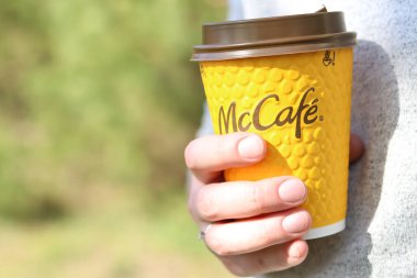 Kyiv, Ukrayna - 21 Nisan 2025: McDonalds 'dan tek kullanımlık kahve kadınların elinde. Doğada bir fincan kahveyle dolaşmak, kahve götürmek. Fast food. Latte veya cappuccino. MK Kafe