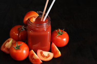 Koyu arkaplanda domates suyu. Sebze diyeti içeceği. Bir bardak dolusu taze domates suyu. Olgun kırmızı domatesler ve onlardan yapılmış meyve suyu. Meyve suyu ve pipetli bardak, domates. Sağlıklı içecek.