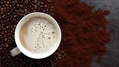 Cappuccino, en iyi manzara. Kahve çekirdekleri ve öğütülmüş kahvenin arasında bir fincan kapuçino. Kavrulmuş kahve çekirdekleri arasında bir fincan aromatik kahve. Canlandırıcı bir içki. Boşluğu kopyala