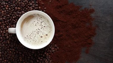 Cappuccino, en iyi manzara. Kahve çekirdekleri ve öğütülmüş kahvenin arasında bir fincan kapuçino. Kavrulmuş kahve çekirdekleri arasında bir fincan aromatik kahve. Canlandırıcı bir içki. Boşluğu kopyala