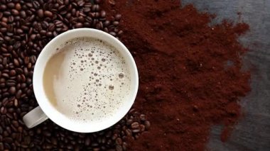 Cappuccino, en iyi manzara. Kahve çekirdekleri ve öğütülmüş kahvenin arasında bir fincan kapuçino. Kavrulmuş kahve çekirdekleri arasında bir fincan aromatik kahve. Canlandırıcı bir içki. Boşluğu kopyala
