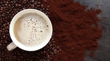 Cappuccino, en iyi manzara. Kahve çekirdekleri ve öğütülmüş kahvenin arasında bir fincan kapuçino. Kavrulmuş kahve çekirdekleri arasında bir fincan aromatik kahve. Canlandırıcı bir içki. Boşluğu kopyala