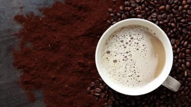 Cappuccino, en iyi manzara. Kahve çekirdekleri ve öğütülmüş kahvenin arasında bir fincan kapuçino. Kavrulmuş kahve çekirdekleri arasında bir fincan aromatik kahve. Canlandırıcı bir içki. Boşluğu kopyala