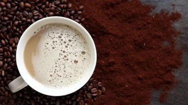 Cappuccino, en iyi manzara. Kahve çekirdekleri ve öğütülmüş kahvenin arasında bir fincan kapuçino. Kavrulmuş kahve çekirdekleri arasında bir fincan aromatik kahve. Canlandırıcı bir içki. Boşluğu kopyala