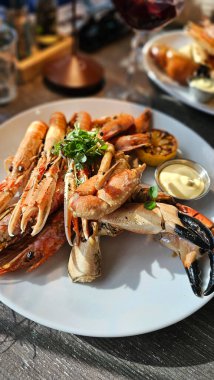 Tabakta, restoranda pişmiş deniz mahsulleri. Soslu ve limonlu kabuklular. Lezzetli ve sağlıklı yiyecekler. Deniz ürünleri tabağının çok güzel bir sunumu. Büyük karidesler, langoustine