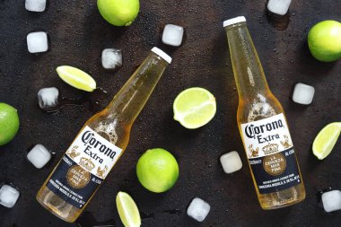 Kyiv, Ukrayna - 10 Mayıs 2025: Ahşap zemin üzerinde limon ve buz küpleri olan ekstra Corona biraları. Corona hafif bir bira. Limonlu bira, üst manzara, boş yer. Koyu bir masada bira.