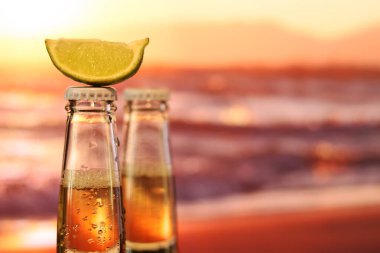 Limonlu bira, gün batımının arka planında. Limonlu bir şişe biraya yakın çekim, seçici odaklanma. Sahilde gün batımı. Tazeleyici içecek. Tatil ve eğlence konsepti