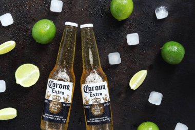 Kyiv, Ukrayna - 10 Mayıs 2025: Ahşap zemin üzerinde limon ve buz küpleri olan ekstra Corona biraları. Corona hafif bir bira. Limonlu bira, üst manzara, boş yer. Koyu bir masada bira.