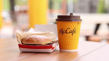 Kyiv, Ukrayna, 12 Mayıs 2025 McDonald 's Latte ve Royal Cheeseburger. Tek kullanımlık bir fincanda hazır kahve. Verandada fast food. Sarı McCafe bardağı karton bir kutunun yanında çizburgerli