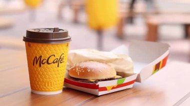 Kyiv, Ukrayna, 12 Mayıs 2025 McDonald 's Latte ve Royal Cheeseburger. Tek kullanımlık bir fincanda hazır kahve. Verandada fast food. Sarı McCafe bardağı karton bir kutunun yanında çizburgerli