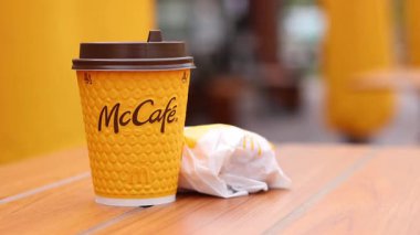 Kyiv, Ukrayna - 12 Mayıs 2025: McDonalds 'da büyük bir latte ve duble çizburger. Tek kullanımlık bir fincanda hazır kahve. Verandadaki bir masada hazır yemek. Sarı McCafe bardağı bir hamburgerin yanında