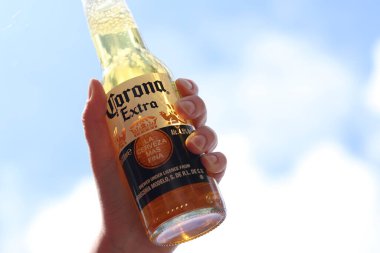 Kyiv, Ukrayna - 12 Mayıs 2025: Bir kadının elinde gökyüzüne karşı fazladan bira. Corona hafif bir bira. Şişe bira. Yakın planda meşrubat. Bir şişe Corona birası, arka ışıklandırma. Rahatlama