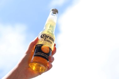 Kyiv, Ukrayna - 12 Mayıs 2025: Bir kadının elinde gökyüzüne karşı fazladan bira. Corona hafif bir bira. Şişe bira. Yakın planda meşrubat. Bir şişe Corona birası, arka ışıklandırma. Rahatlama