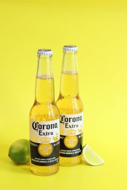Kyiv, Ukrayna - 10 Mayıs 2025: Sarı arka planda Corona Ekstra birası. Corona hafif bir bira. Limonlu şişe bira, yan görüş, boş yer. Parlak bir arka planda alkollü içki
