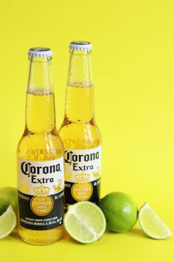 Kyiv, Ukrayna - 10 Mayıs 2025: Sarı arka planda Corona Ekstra birası. Corona hafif bir bira. Limonlu şişe bira, yan görüş, boş yer. Parlak bir arka planda alkollü içki