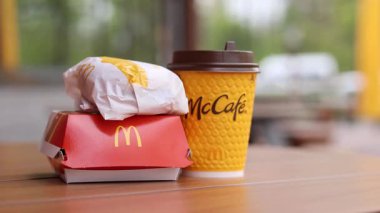 Kyiv, Ukrayna - 12 Mayıs 2025: McDonald 's Latte, Royal Cheeseburger ve Double Cheeseburger verandada. Sarı McCafe bardağı diğer fast food bardaklarının yanında. Çizburger ve kahve.
