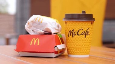 Kyiv, Ukrayna - 12 Mayıs 2025: McDonald 's Latte, Royal Cheeseburger ve Double Cheeseburger verandada. Sarı McCafe bardağı diğer fast food bardaklarının yanında. Çizburger ve kahve.