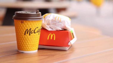 Kyiv, Ukrayna - 12 Mayıs 2025: McDonald 's Latte, Royal Cheeseburger ve Double Cheeseburger verandada. Sarı McCafe bardağı diğer fast food bardaklarının yanında. Çizburger ve kahve.