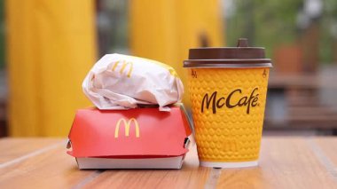 Kyiv, Ukrayna - 12 Mayıs 2025: McDonald 's Latte, Royal Cheeseburger ve Double Cheeseburger verandada. Sarı McCafe bardağı diğer fast food bardaklarının yanında. Çizburger ve kahve.