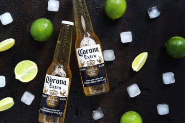 Kyiv, Ukrayna - 10 Mayıs 2025: Ahşap zemin üzerinde limon ve buz küpleri olan ekstra Corona biraları. Corona hafif bir bira. Limonlu bira, üst manzara, boş yer. Koyu bir masada bira.