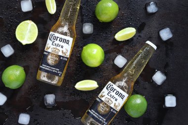 Kyiv, Ukrayna - 10 Mayıs 2025: Ahşap zemin üzerinde limon ve buz küpleri olan ekstra Corona biraları. Corona hafif bir bira. Limonlu bira, üst manzara, boş yer. Koyu bir masada bira.