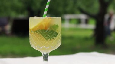 Sıcak bir yaz gününde bahçe masasında iç. Dışarıdaki ahşap bir masada kokteylli cam. Bulanık doğanın arka planına karşı bir masada limonata. Bardakta limonata ya da başka bir içecek.