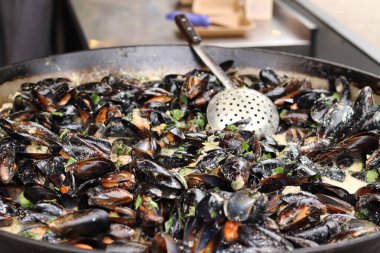 Büyük bir tavada maydanozlu ve soslu midye. Yemek katı. Sokak yemeği. Kabuklu midyeler kızartma tavasında otlarla pişiriliyor. Bir markette sosta pişirilmiş midyeler. Deniz ürünleri tabağı pişiriyorum.