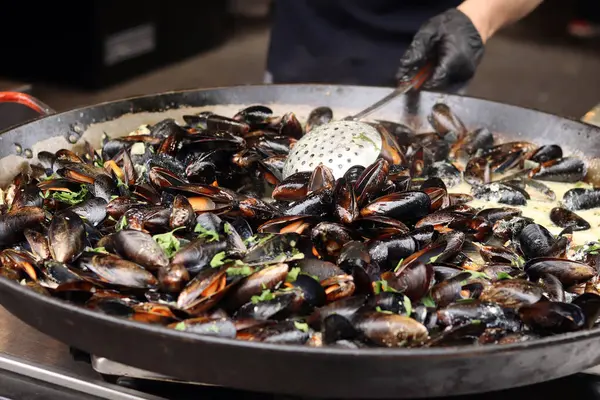 Büyük bir tavada maydanozlu ve soslu midye. Yemek katı. Sokak yemeği. Kabuklu midyeler kızartma tavasında otlarla pişiriliyor. Bir markette sosta pişirilmiş midyeler. Deniz ürünleri tabağı pişiriyorum.