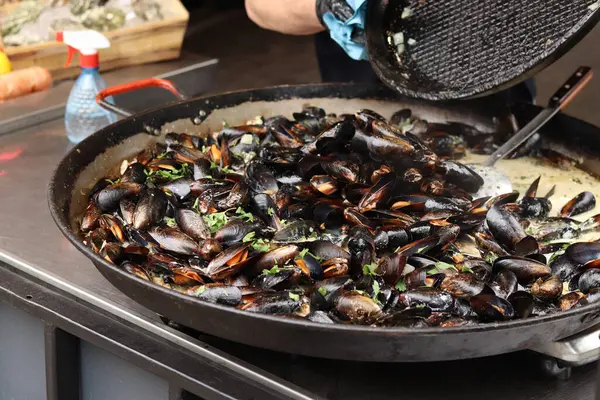 Büyük bir tavada maydanozlu ve soslu midye. Yemek katı. Sokak yemeği. Kabuklu midyeler kızartma tavasında otlarla pişiriliyor. Bir markette sosta pişirilmiş midyeler. Deniz ürünleri tabağı pişiriyorum.