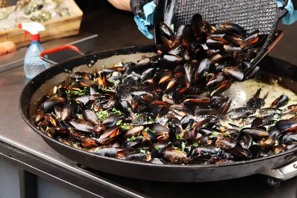 Büyük bir tavada maydanozlu ve soslu midye. Yemek katı. Sokak yemeği. Kabuklu midyeler kızartma tavasında otlarla pişiriliyor. Bir markette sosta pişirilmiş midyeler. Deniz ürünleri tabağı pişiriyorum.