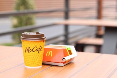 Kyiv, Ukrayna - 12 Mayıs 2025: Sarı McCafe bardağı karton bir çizburgerin yanında. McDonald 's Latte ve Royal Cheeseburger. Tek kullanımlık bir fincanda hazır kahve. Verandada fast food.
