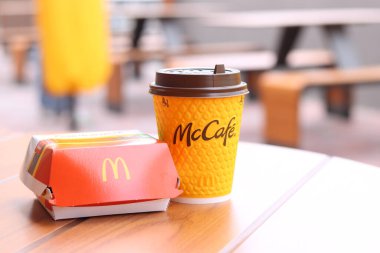 Kyiv, Ukrayna - 12 Mayıs 2025: Sarı McCafe bardağı karton bir çizburgerin yanında. McDonald 's Latte ve Royal Cheeseburger. Tek kullanımlık bir fincanda hazır kahve. Verandada fast food.