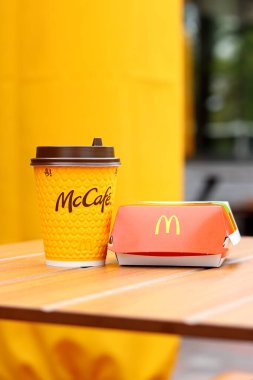 Kyiv, Ukrayna - 12 Mayıs 2025: Sarı McCafe bardağı karton bir çizburgerin yanında. McDonald 's Latte ve Royal Cheeseburger. Tek kullanımlık bir fincanda hazır kahve. Verandada fast food.