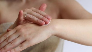 El kremi. Genç bir kadının eline nemlendirici kremle yakın çekim. Cilt bakımı. Havlu giymiş kadın el derisine krem sürüyor. Sağlıklı cilt. Kozmetoloji. Günlük rutin