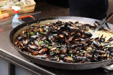 Büyük bir tavada maydanozlu ve soslu midye. Yemek katı. Sokak yemeği. Kabuklu midyeler kızartma tavasında otlarla pişiriliyor. Bir markette sosta pişirilmiş midyeler. Deniz ürünleri tabağı pişiriyorum.