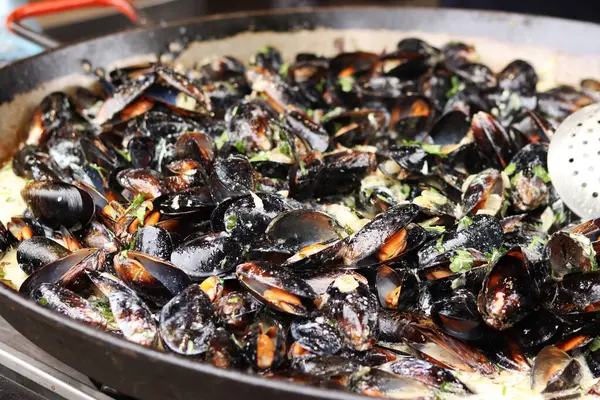 Büyük bir tavada maydanozlu ve soslu midye. Yemek katı. Sokak yemeği. Kabuklu midyeler kızartma tavasında otlarla pişiriliyor. Bir markette sosta pişirilmiş midyeler. Deniz ürünleri tabağı pişiriyorum.