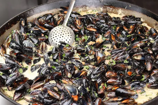 Büyük bir tavada maydanozlu ve soslu midye. Yemek katı. Sokak yemeği. Kabuklu midyeler kızartma tavasında otlarla pişiriliyor. Bir markette sosta pişirilmiş midyeler. Deniz ürünleri tabağı pişiriyorum.