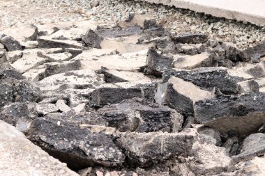 Asfalt yolda büyük parçalara ayrıldı. Şehirdeki tamirat işleri. Yol onarımı. Asfalt kaldırımlardan oluşan bir dağ. Tamir konsepti. Bir asfalt enkazı yığını. Yakın plan.