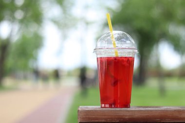 Tek kullanımlık plastik bardakta limonata, paket içecek. Yazın bir parkın arka planına karşı ferahlatıcı bir içecek. Ahududu ve limonlu pembe limonata. Tek kullanımlık bir bardakta içkinin yakın plan çekimi.